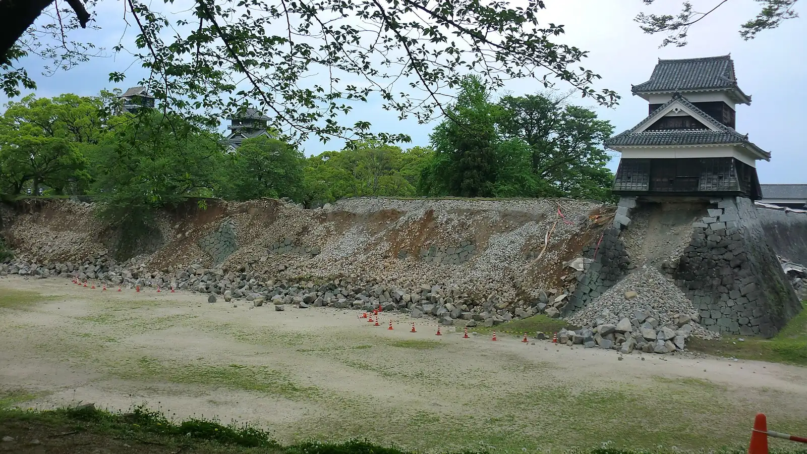 熊本城の石垣が崩れ、石材が手前の広場に散らばっている。右端の櫓は、崩れ残った隅の石垣で支えられている