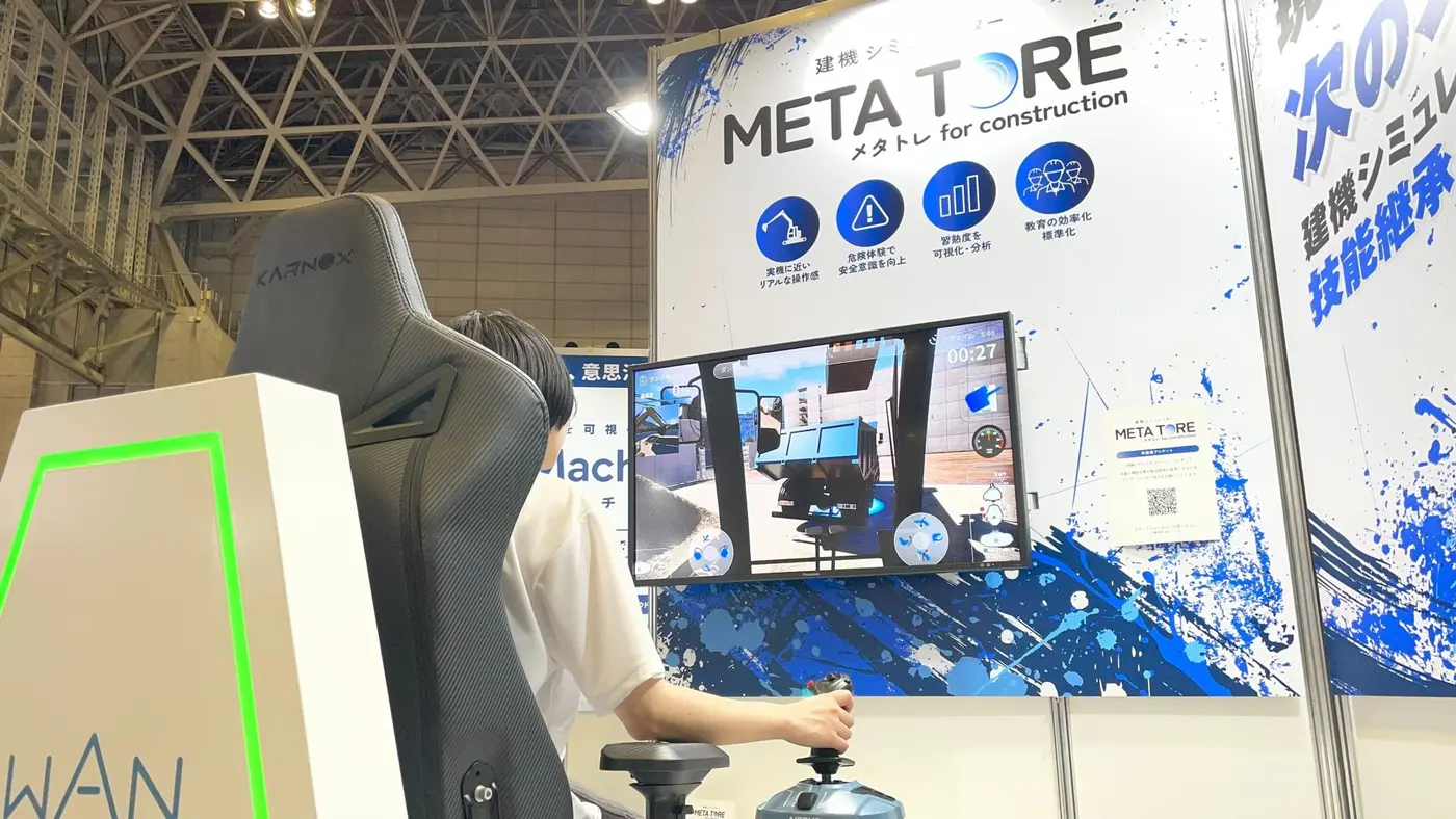 展示会のメタトレのブースで、モニターに映したショベルの運転席の視点を見ながら、レバーで操作している体験者